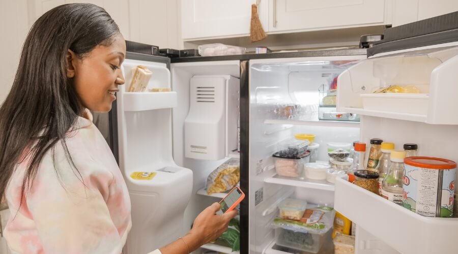 A woman holding a cell phone in front of the fridge
